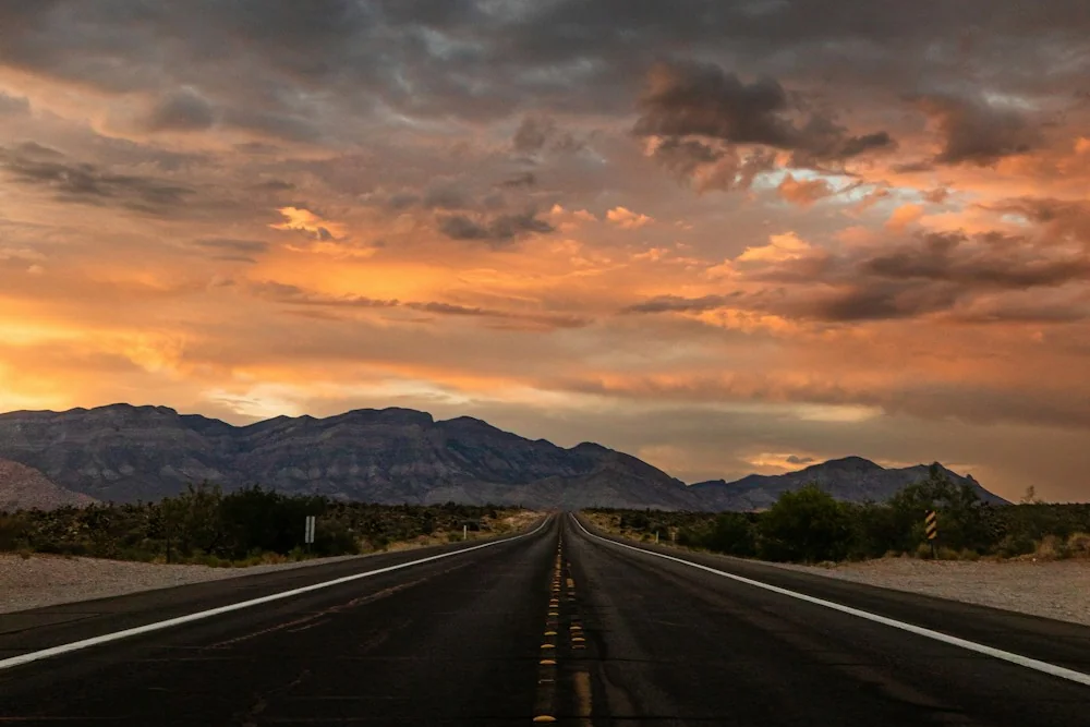 An open desert highway beneath a dramatic sunset
